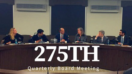 Six adults sitting behind a long round desk with the title "275th Quarterly Board Meeting" layered on top