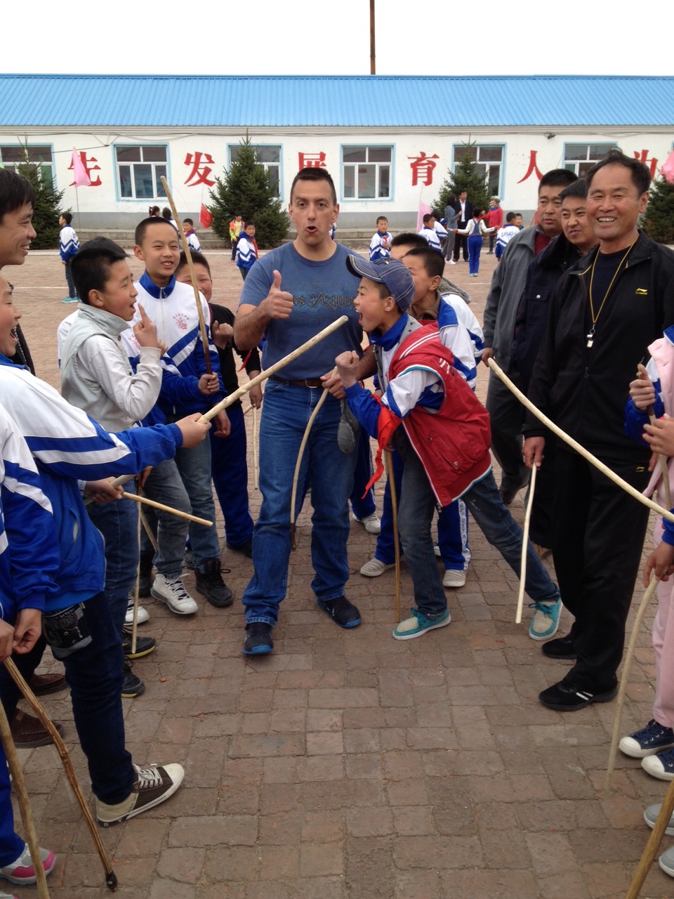 An American participant teaches Native American games to a group of Chinese boys during an outdoor activity.