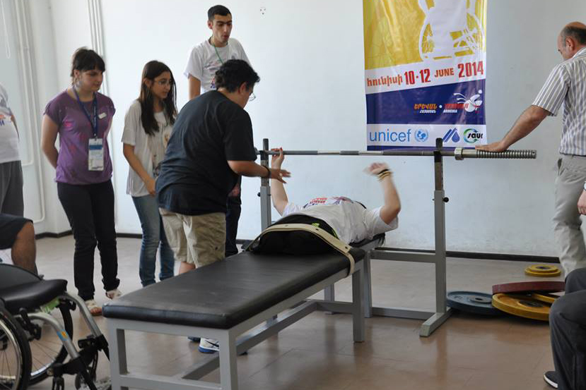 An American participant assists an athlete with their bench press. 