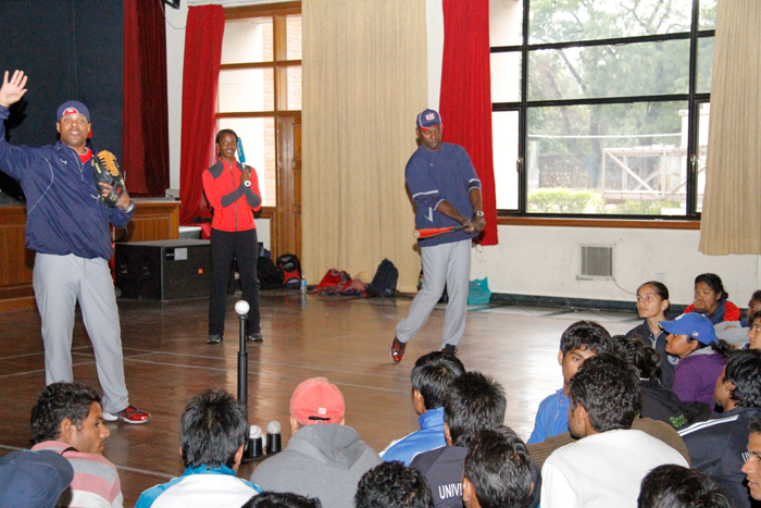 Natasha Watley, Barry Larkin, and Joe Logan teach batting skills indoors while highlighting the differences between batting in baseball and softball. 