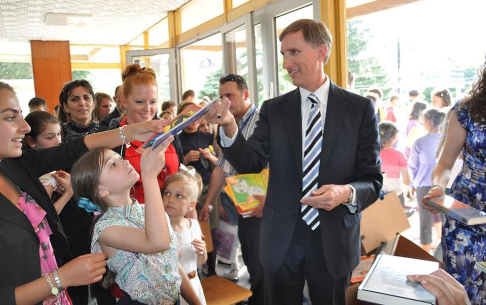 Fulbright English Teaching Assistant Jennifer Birdsall (in red) with U.S. Ambassador to Macedonia Paul Wholers as he hands donated English children's books out to local children at the American Corner Tetovo.