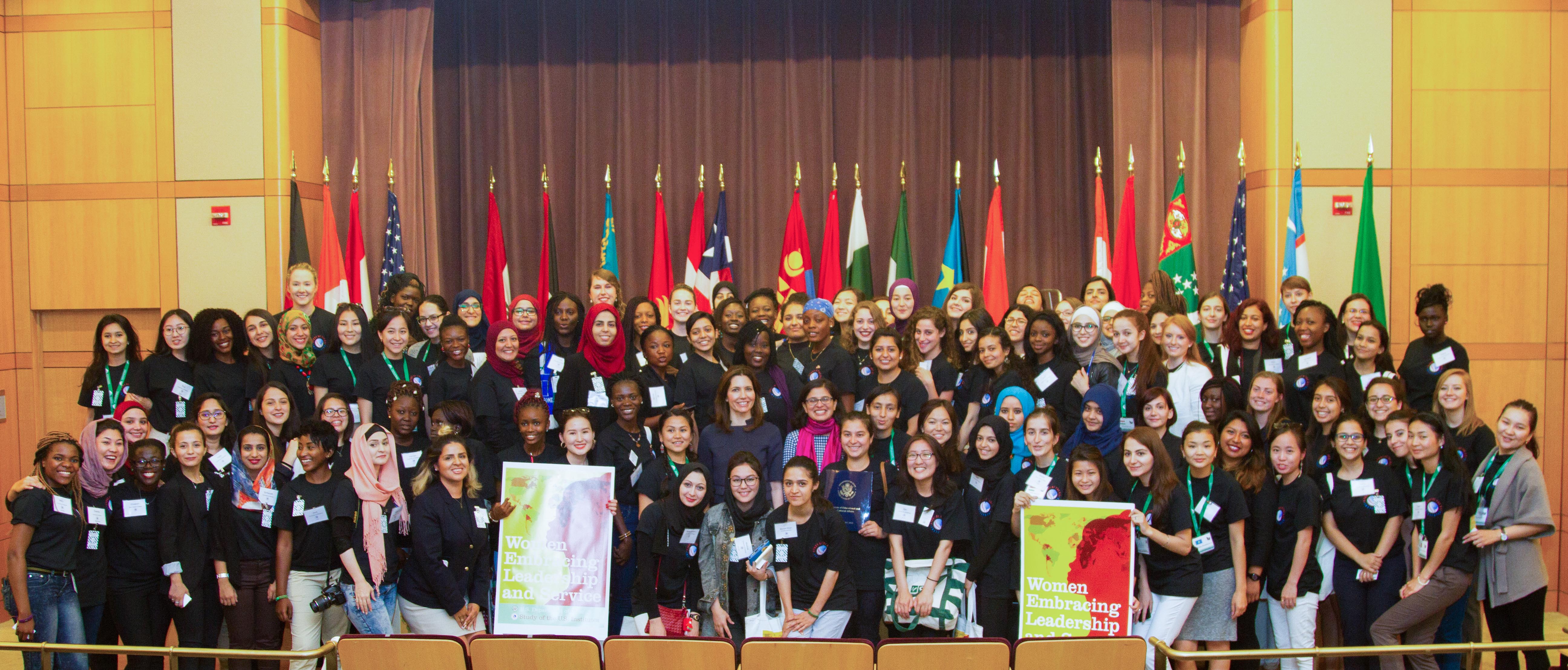 International group of women pose for a group shot in front of flags
