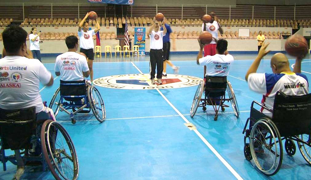 Wheelchair bound participants on the court holding basketballs while learning from the former NBA players