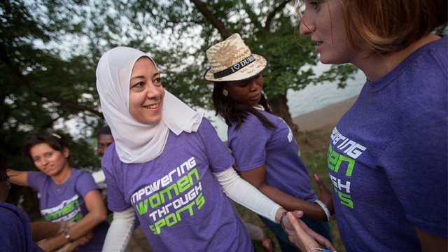 Girl in white headscarf wearing purple tee shirt shaking hands with another girl in a matching shirt 