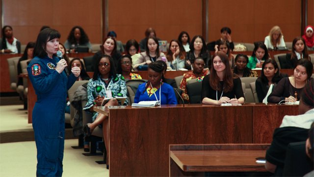 Female NASA astronaut speaking to a group of women in a lecture hall. 