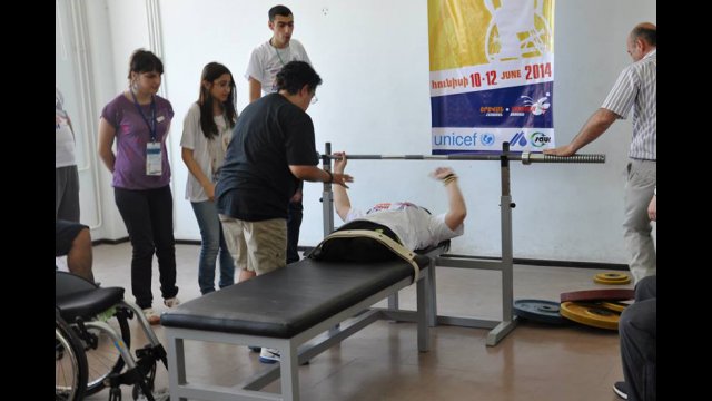 An American participant assists an athlete with their bench press. 