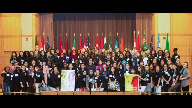 International group of women pose for a group shot in front of flags