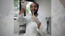 Man in lab coat holds sticks above a vile that has long clear sticky substance hanging from the stick into the vile