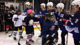 Young women hockey players dressed in gear on an ice rink high five a line of young girls in hockey gear as they enter the rink