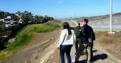Two people standing on hill look at field a ranger is pointing towards