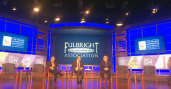 Three men sit on stage with Fulbright Association graphic on screen in background