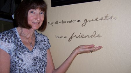 Photo of Anita Bevan next to plaque saying "May all who enter as guests leave as friends." Photo of Anita Bevan next to plaque saying "May all who enter as guests leave as friends."